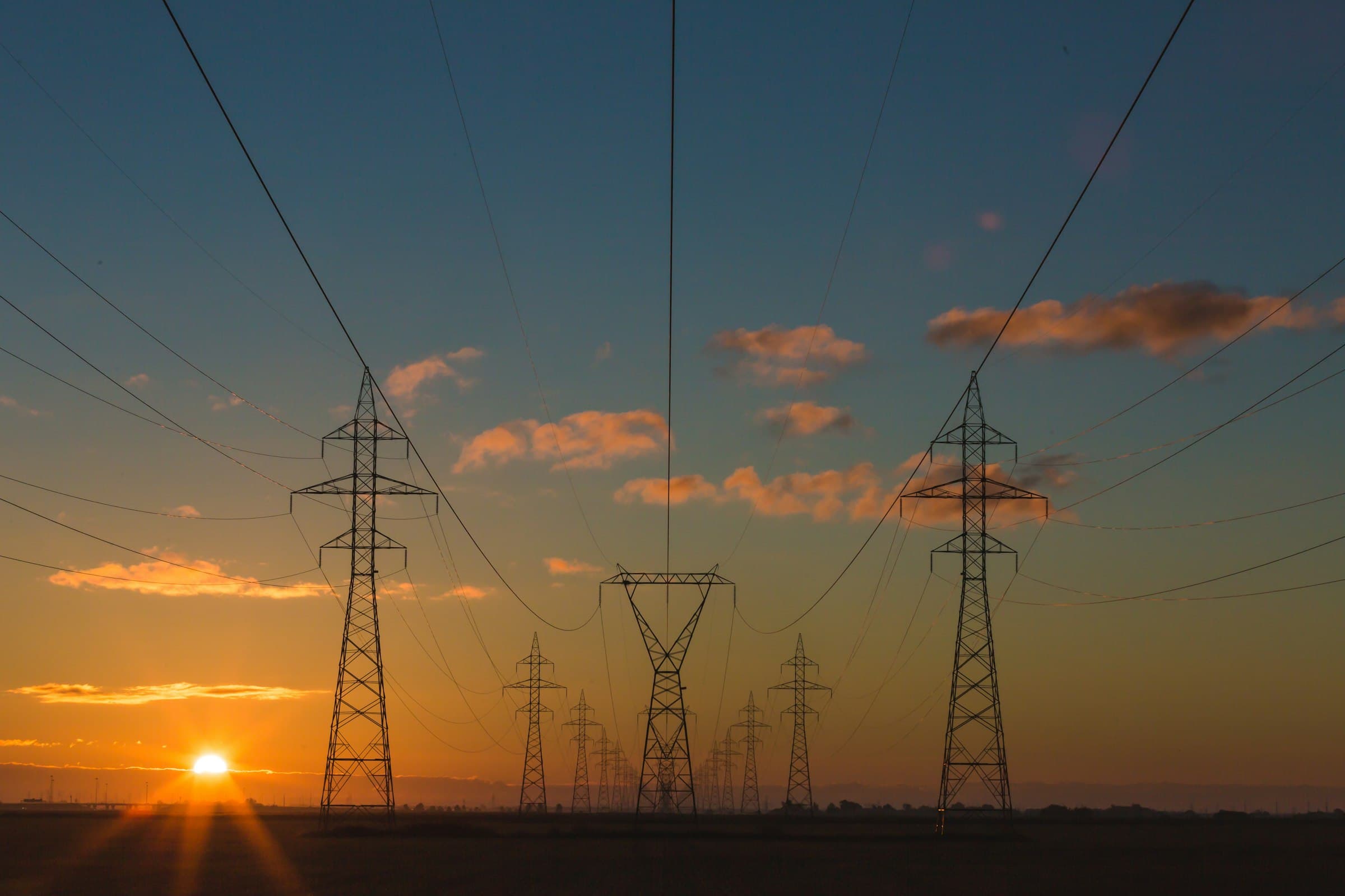 Transmission towers carrying power lines toward a low evening sun